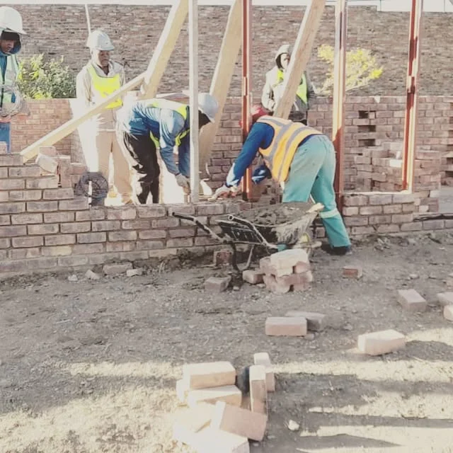 Bricklayers in hard hats building walls between window frames